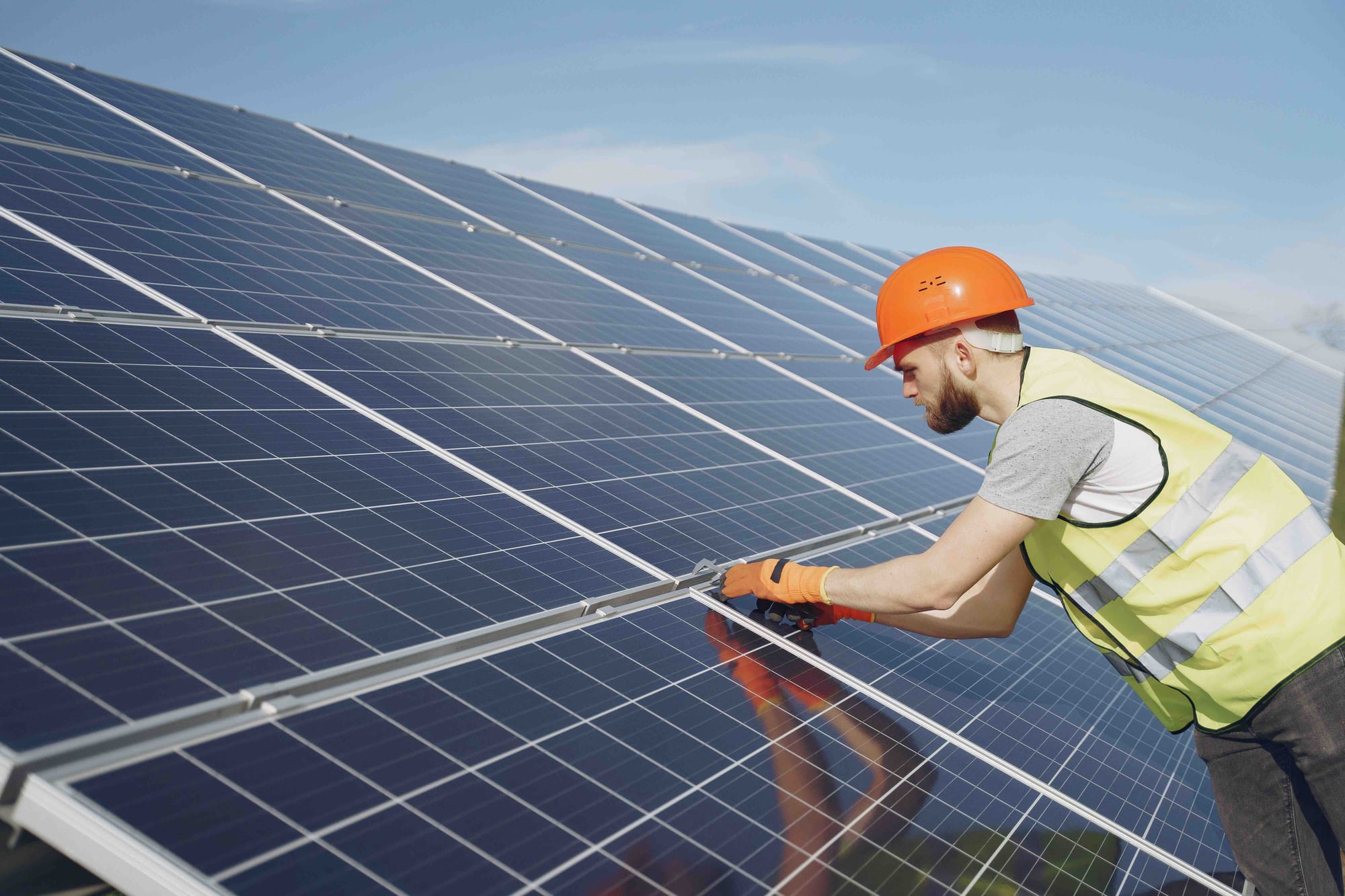 A man in a hi-vis vest and orange helmet, fitting solar panels.