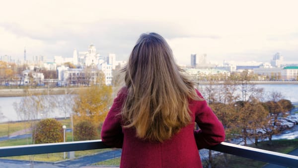 Rear view of woman standing on balcony and enjoying the view on the city. Back view of young woman